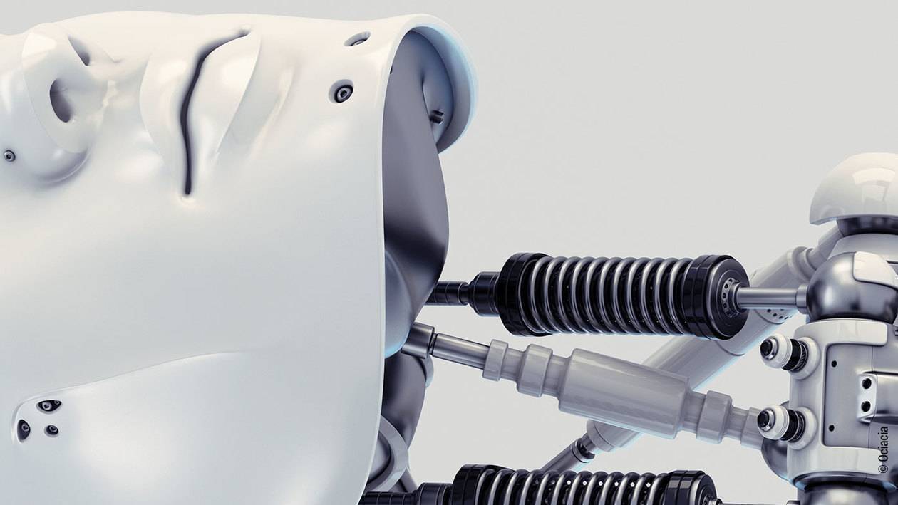 Foto: Ein liegender Roboter mit menschlichen Gesichtszügen und einer offen sichtbaren Hydraulik am Hals.