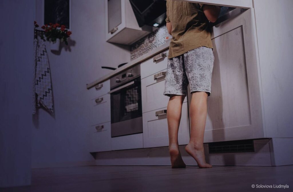 Foto: Ein Mensch steht barfuß in der nächtlichen Küche und schaut in den Kühlschrank