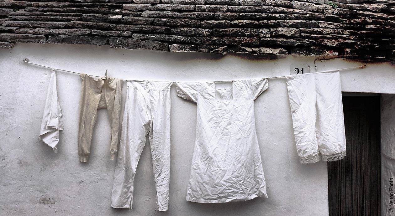 Foto: Vor einer einfachen Hütte hängt eine Wäscheleine mit Nachthemden und Pyjama in Weiß- und Beigetönen.