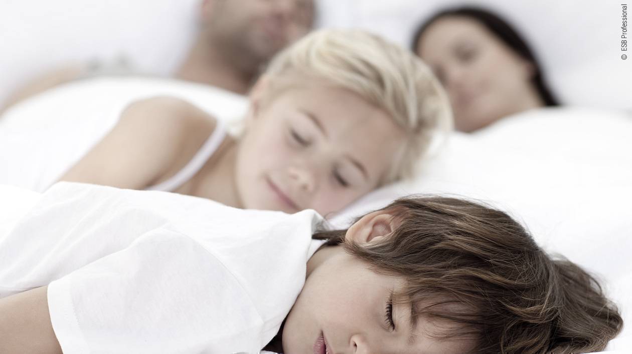 Foto: Zwei Kinder liegen schlafend mit ihren Eltern im Familienbett.