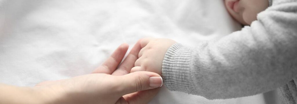 Foto: Mutter und Kind halten Händchen im Familienbett.