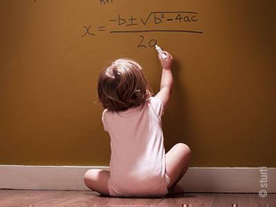 Foto: Ein Baby sitzt einer Wand zugewandt und malt an diese mit erhobenem Stift eine komplizierte mathematische Formel.