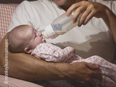 Foto: Ein Baby liegt im Arm einer männlichen Person und wird mit der Flasche gefüttert.