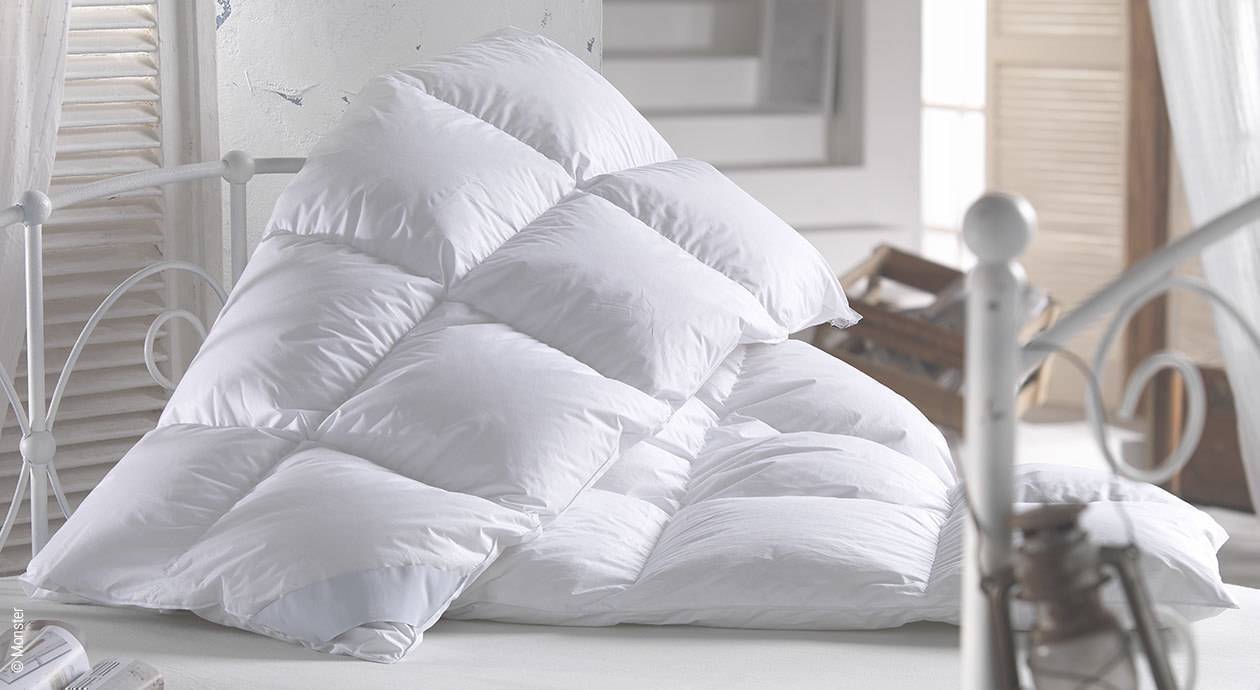 Foto: Eine weiße Daunendecke liegt unordentlich auf einem Bett