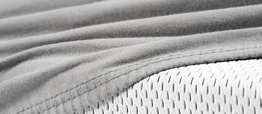 Foto: Ein Ausschnitt des grauen BODYGUARD® Jersey-Spannbettlakens, das über die BODYGUARD® Matratze gezogen wird.