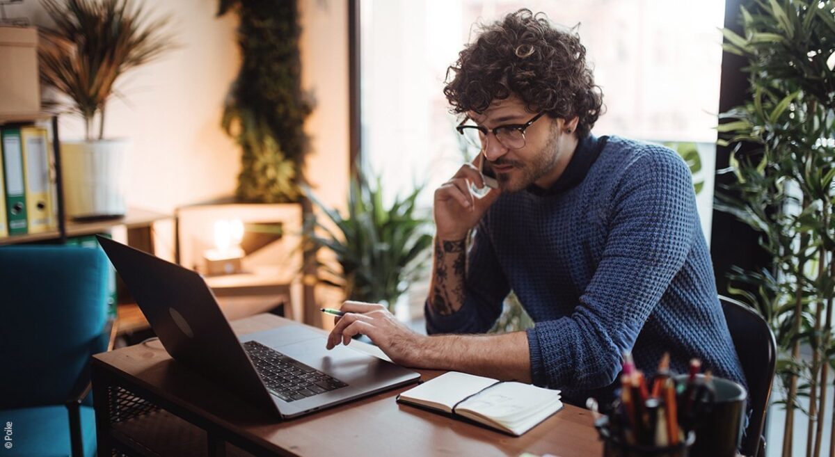 Foto: Ein Mann arbeitet zuhause an einem Laptop und telefoniert dabei.