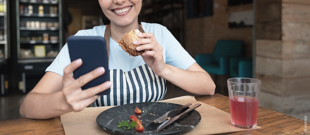alt="Foto: Eine Person in Arbeitschürze sitzt essend an einem Restauranttisch.