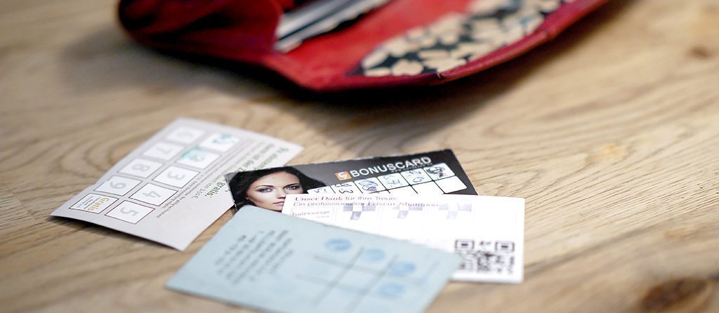 Foto: Ein geöffnetes Portemonnaie liegt auf einem Holztisch. Davor sind diverse Rabbat- und Bonuskarten verteilt.