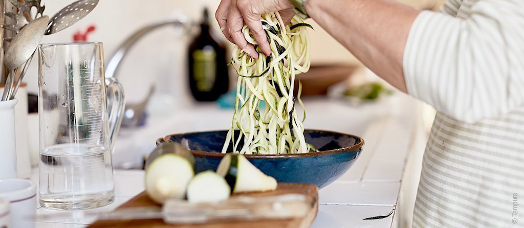 Foto: In der Küche bereiten zwei Hände Zucchininudeln, Zoodles, in einer Pfanne zu – auch gesunde Ernährung kann das Immunsystem stärken.