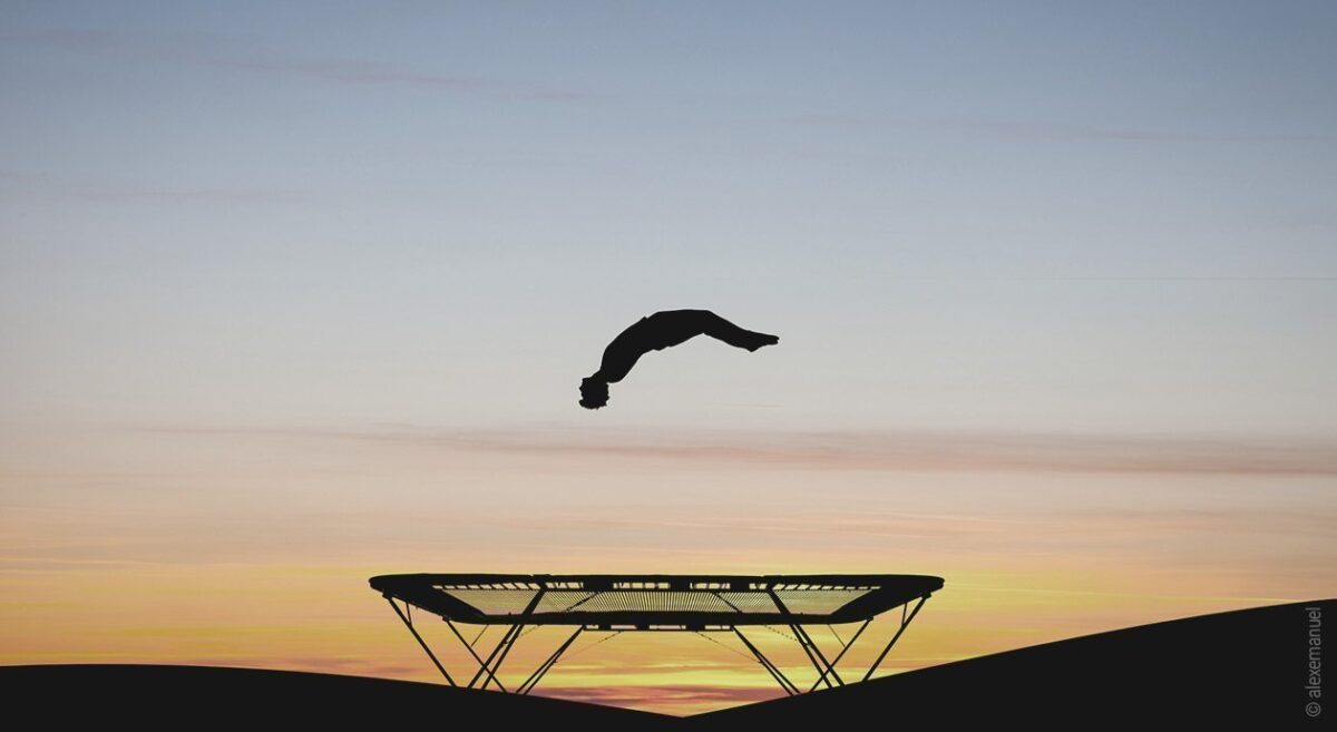 Foto: Vor einem Sonnenuntergang sind die Umrisse einer Person zu erkennen, die liegend über einem Trampolin zu schweben scheint – das symbolisiert den REM-Rebound.