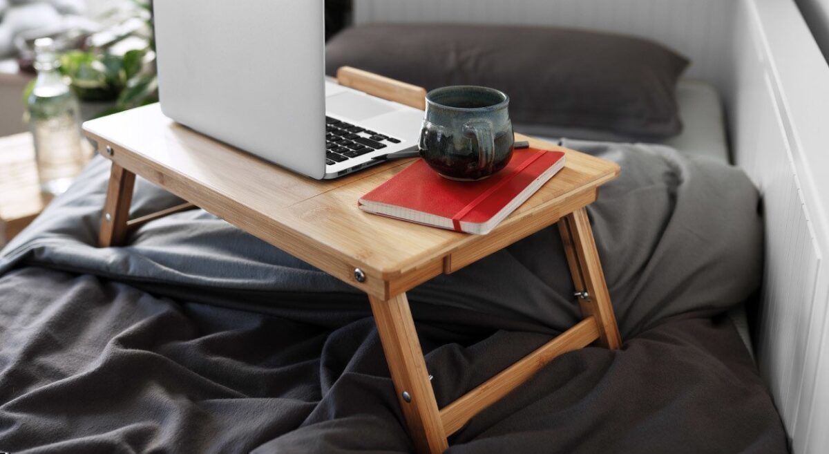 Foto: Ein Betttablett aus Holz mit einem Laptop und einer Kaffeetasse steht auf dem Bett.