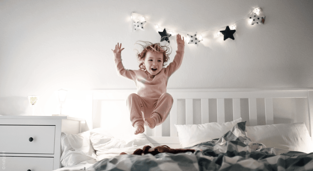 Symbolfoto Betthupferl: ein Kind hüpft auf einem Bett.