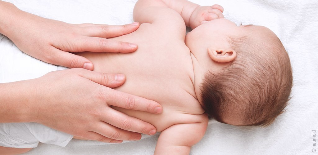 Ein Baby liegt nur mit Windel bekleidet ausgestreckt auf dem Bauch. Zwei Hände massieren den Rücken.
