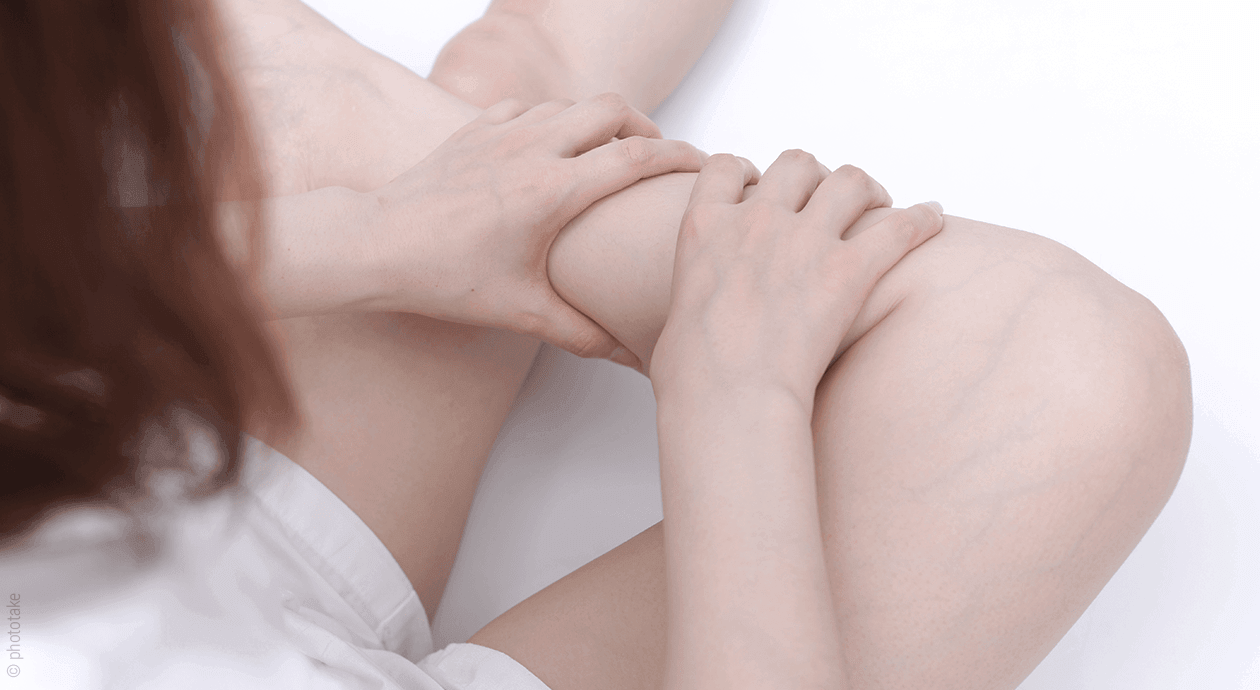 Foto: Eine Person sitzt im Bett und umklammert mit beiden Händen ihre Wade