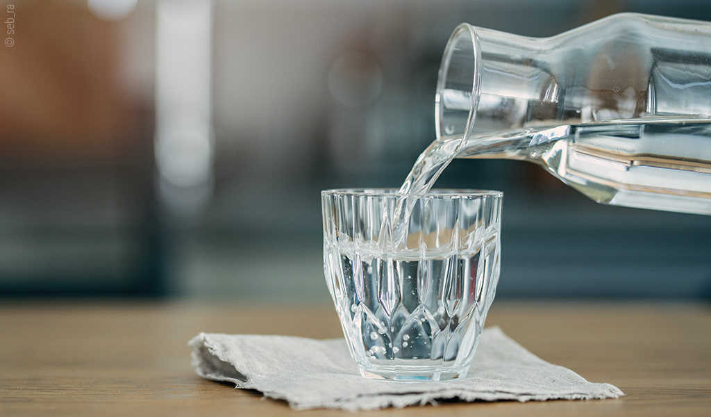 Foto: Aus einer Glaskaraffe wird Wasser in ein Glas geschüttet.
