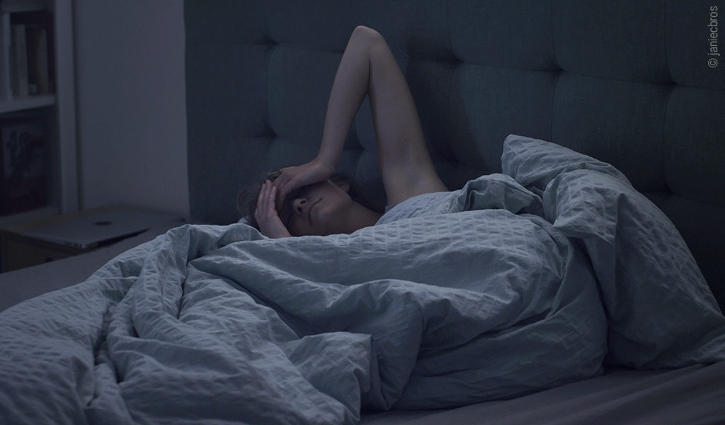 Foto: Eine Person liegt im Bett und hält ihre Hände an die Stirn.