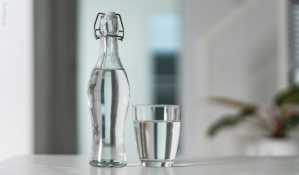 Foto: Eine Glasflasche mit Wasser, daneben steht ein mit Wasser gefülltes Glas.