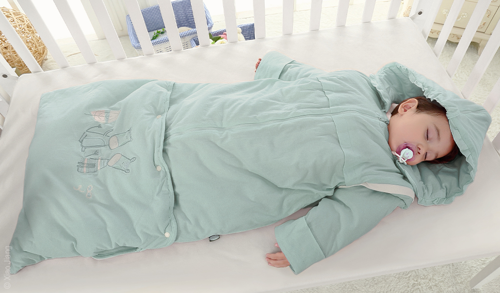 Foto: Ein Kind liegt in einem Babyschlafsack mit Vorrichtung zum nächtlichen Wickeln in einem Kinderbett.