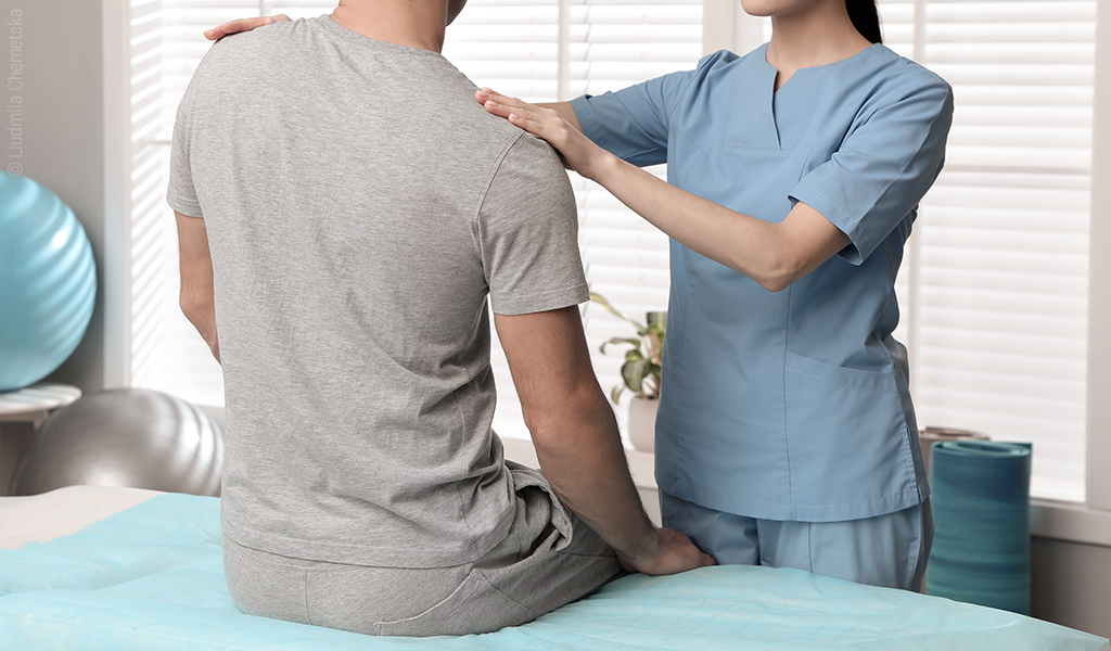 Foto: Die Schultern einer Person werden von einer anderen Person in blauer medizinischer Berufsbekleidung abgetastet.