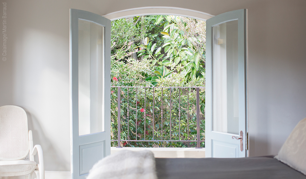 Foto: Eine weit geöffnete Flügeltür in einem weißgehaltenen Raum gibt den Blick nach draußen auf grüne Bäume und Büsche frei