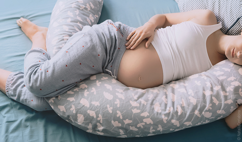 Foto: Eine schwangere Person in Seitenlage, die ihren Schwangerschaftsbauch auf einem Seitenschläferkissen abstützt.