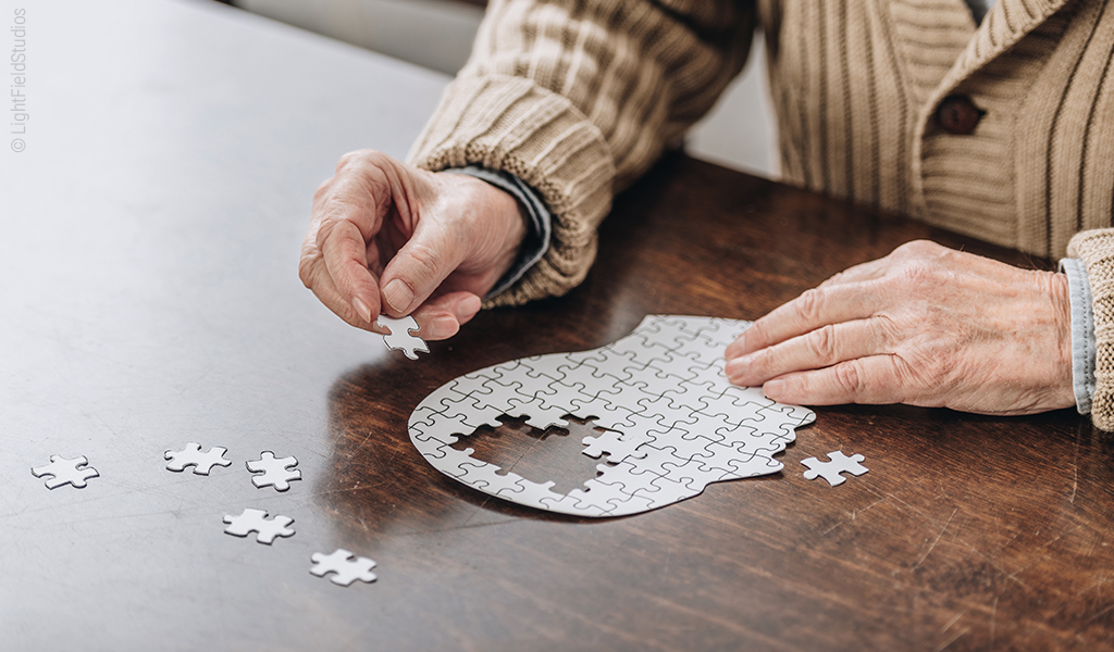 Foto: Zwei ältere Hände puzzeln ein Puzzle in Kopfform.