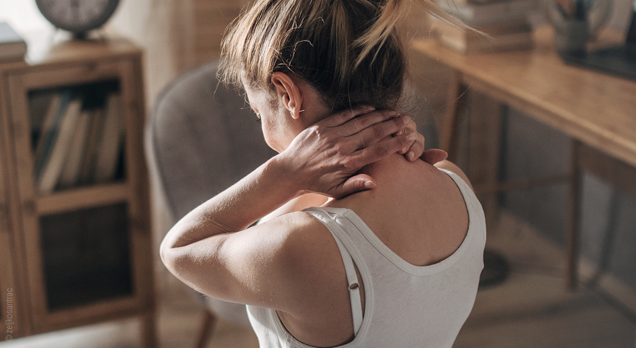 Symbolbild Nackenschmerzen: Eine Person fasst sich mit beiden Händen an den Nacken.