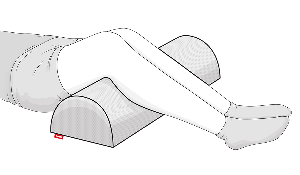 Illustration: Unterkörper einer Person in Rückenlage. Ihre Beine sind leicht angewinkelt über ein längliches, halbrundes Kissen mit rotem bett1-Etikett gelegt.