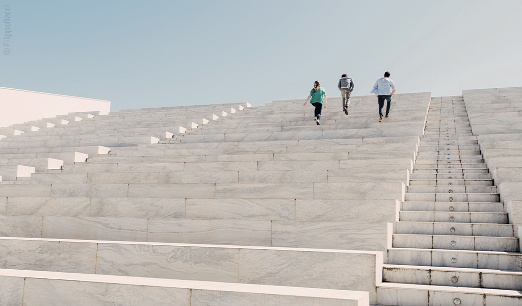 Foto aus Froschperspektive: Drei Personen laufen eine große Treppe empor.
