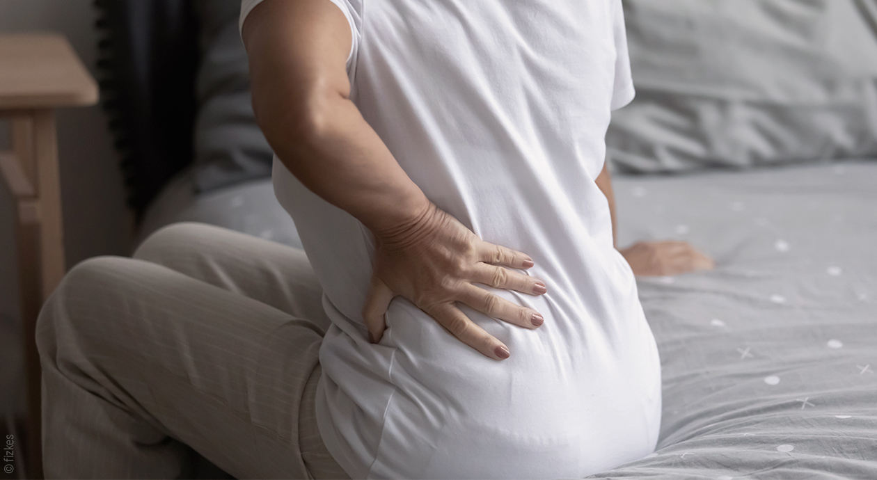 Eine Person sitzt im Bett und hält sich eine Hand an den Rücken