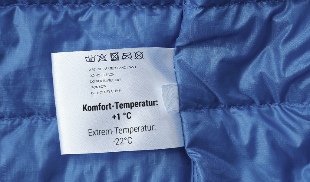 Pflegehinweise und Temperaturangaben auf einem Etikett in einem blauen Schlafsack. Text: Komfort-Temperatur +1 °C, Extrem-Temperatur -22 °C