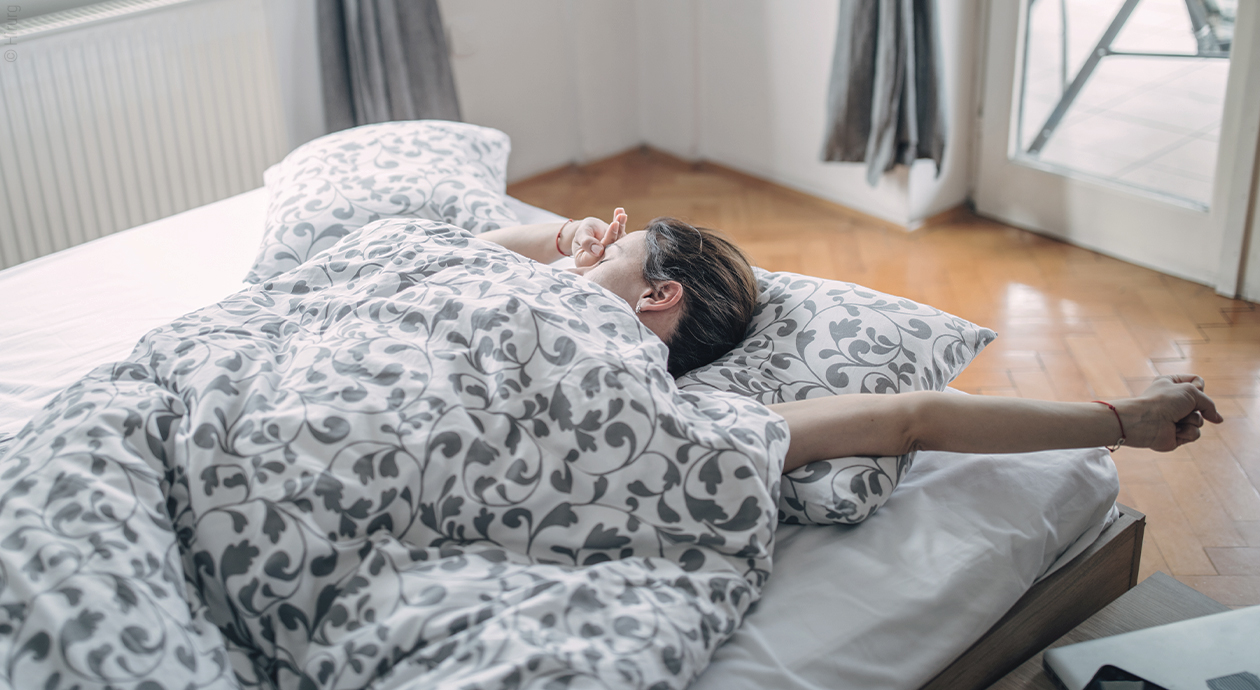 Titelfoto Gute Matratzen: Eine Person liegt im Bett, rekelt sich und streckt einen Arm aus.