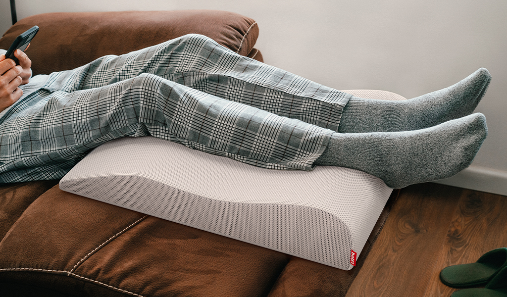 Foto: Eine Person liegt auf dem Sofa. Unter ihren Beinen das BODYGUARD Venenkissen.