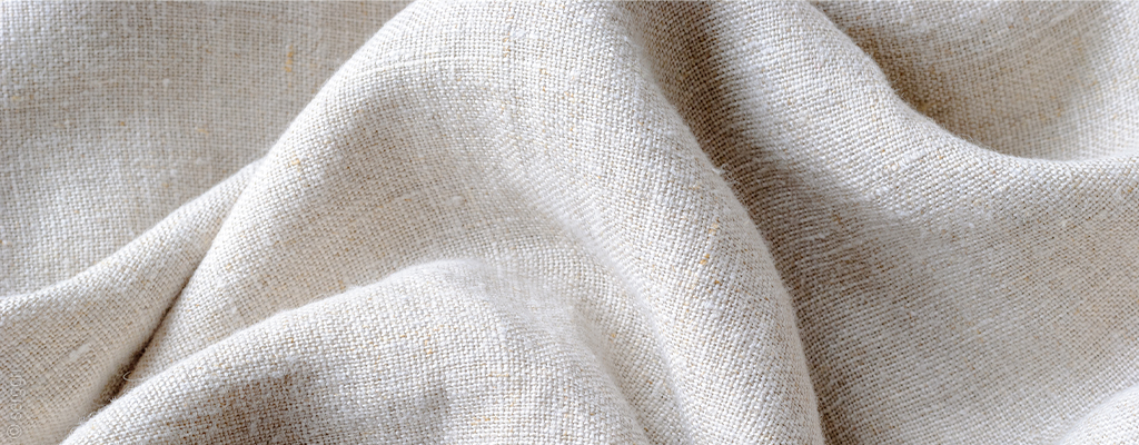 Foto: Nahaufnahme von Leinen-Bettwäsche. Das Bettwäsche Material ist weiß und grobfaserig.