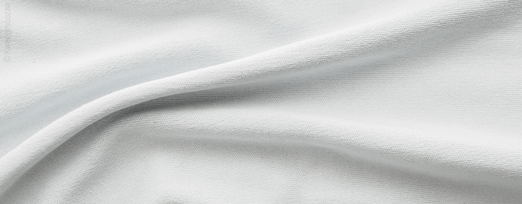 Foto: Nahaufnahme von Mikrofaser-Bettwäsche. Das Bettwäsche Material ist weiß, glatt und sehr feinmaschig.