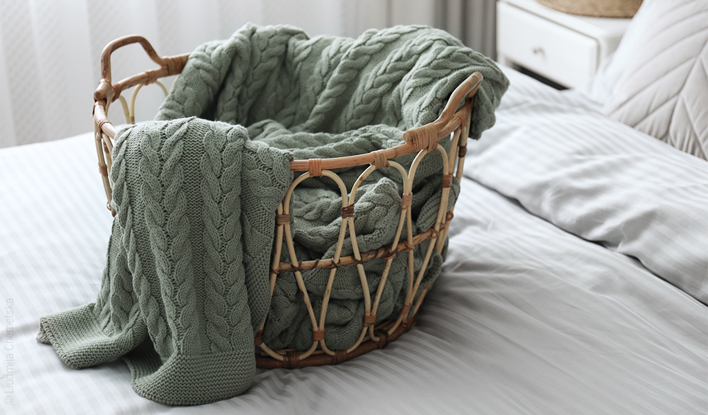 Foto: Auf einem Einzelbett steht ein geflochtener Korb, darin liegt eine Tagesdecke. 
