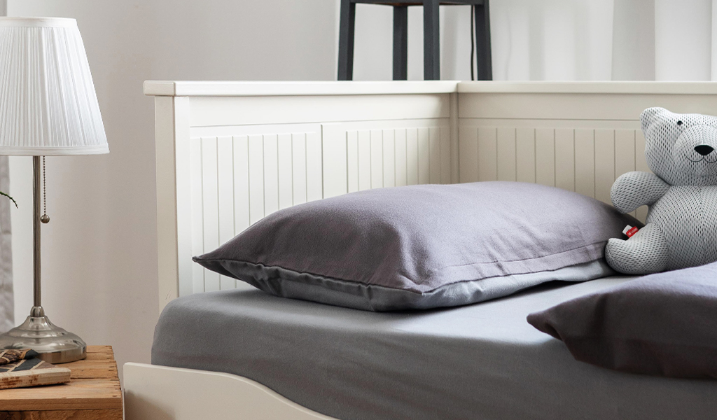 Jugendbett mit BODYGUARD Flanell-Bettwäsche im schlichten Design. Auf dem Bett sitzt der BUDDYGUARD Teddybär.